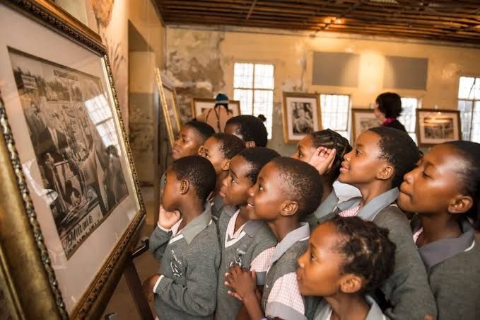 Group of school children in uniform attentively looking at framed photographs in an art gallery.