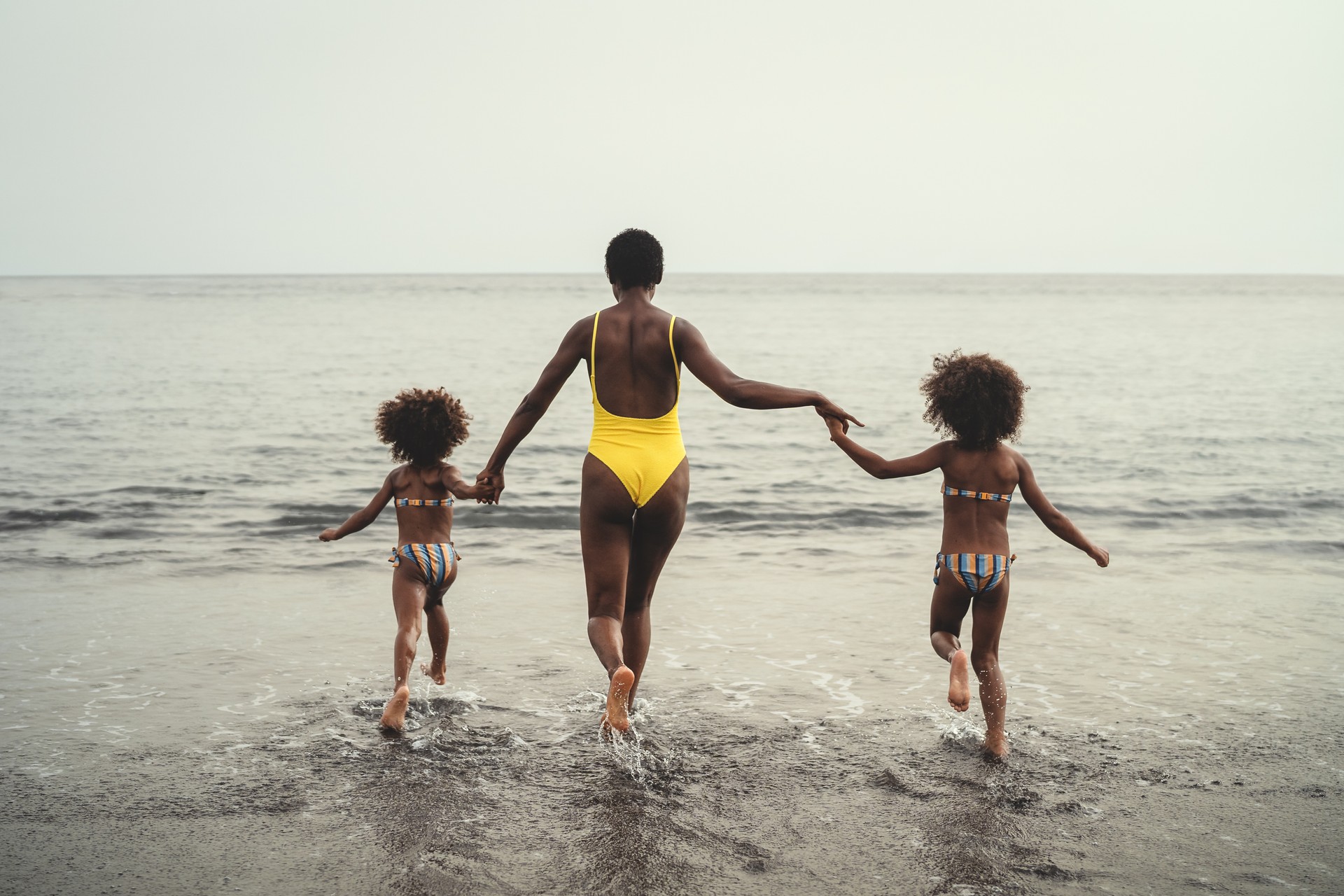 Happy African family running on the beach during summer holidays - Afro American people having fun on vacation time - Parents love and travel lifestyle concept